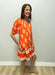 Woman wearing an orange floral dress against a white wall.