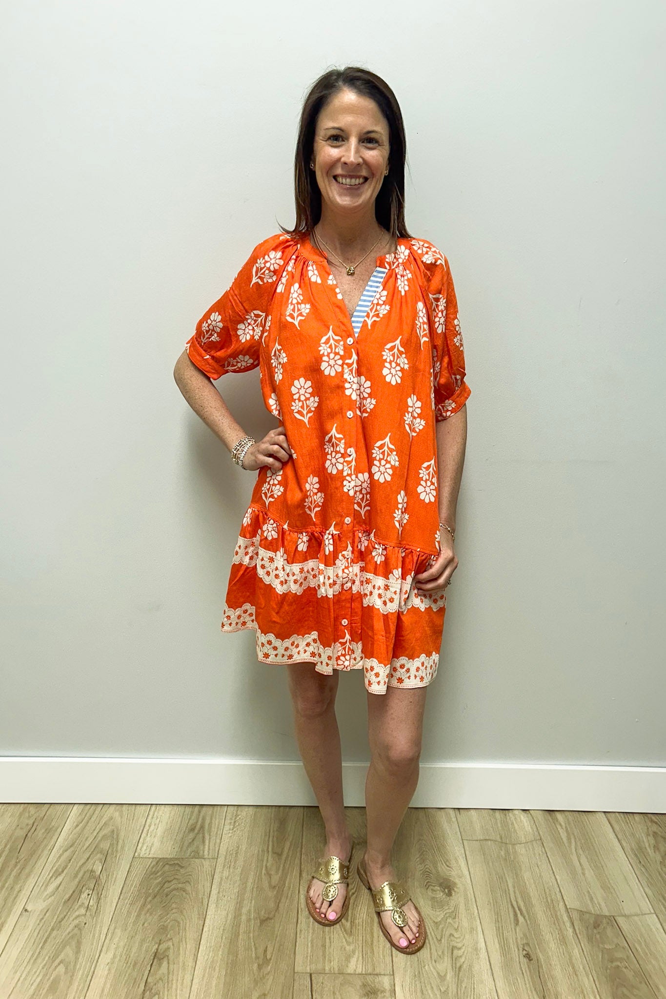Woman wearing an orange floral dress against a white wall.