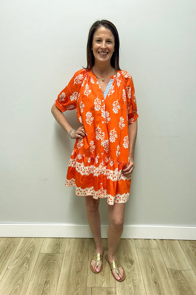 Woman wearing an orange floral dress against a white wall.