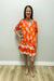 Woman wearing an orange floral dress against a white wall.