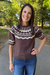 A woman wearing a brown short-sleeve knit sweater with a cream Nordic-style yoke pattern, standing outdoors on a paved path with trees in the background.
