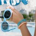Hand holding blue sunglasses with a blurred poolside background