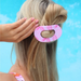pink hair clip in blonde hair model against blue background