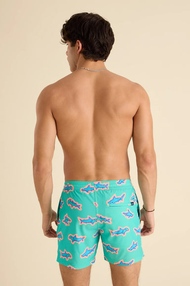 Man wearing teal swim shorts with shark pattern on a beige background