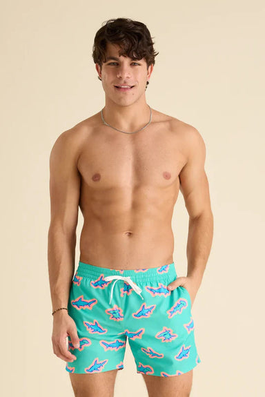 Man wearing teal swim shorts with shark pattern on a beige background