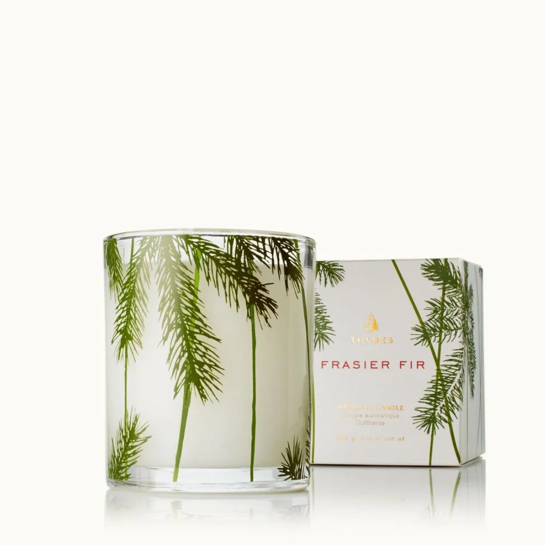 A clear glass jar candle with white wax and green fraser fir tree illustrations, shown next to its white box with matching green and gold fraser fir artwork. The brand name 'VIVID' is visible on the box.