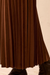 Close-up of a brown pleated skirt with a soft suede-like texture, paired with black boots against a light beige background.