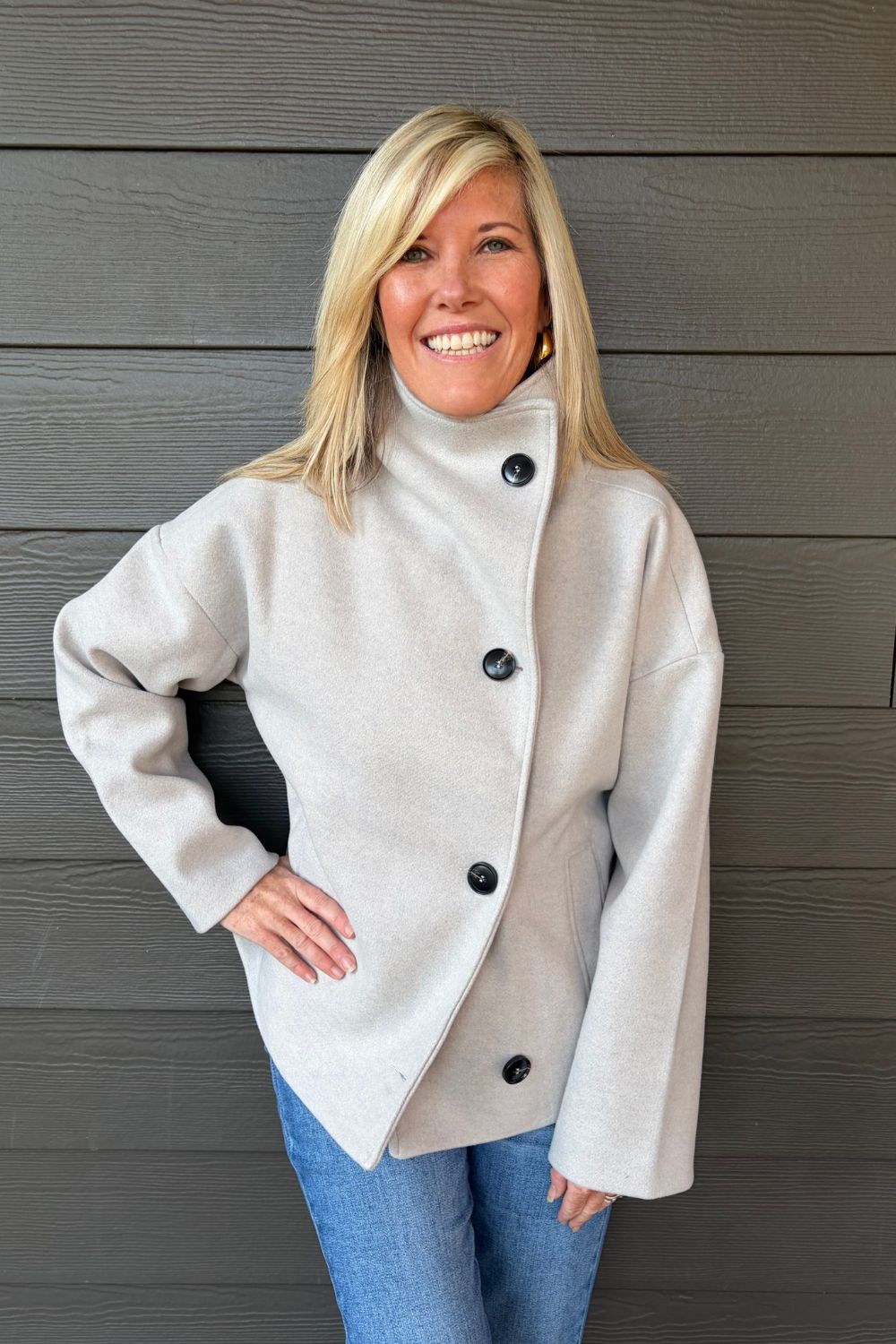 Woman wearing Tribal Sportswear Lofty Chic Funnel Neck Jacket In Antique White with jeans on a dark wood background.