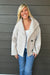 Woman wearing Tribal Sportswear Lofty Chic Funnel Neck Jacket In Antique White with jeans on a dark wood background.