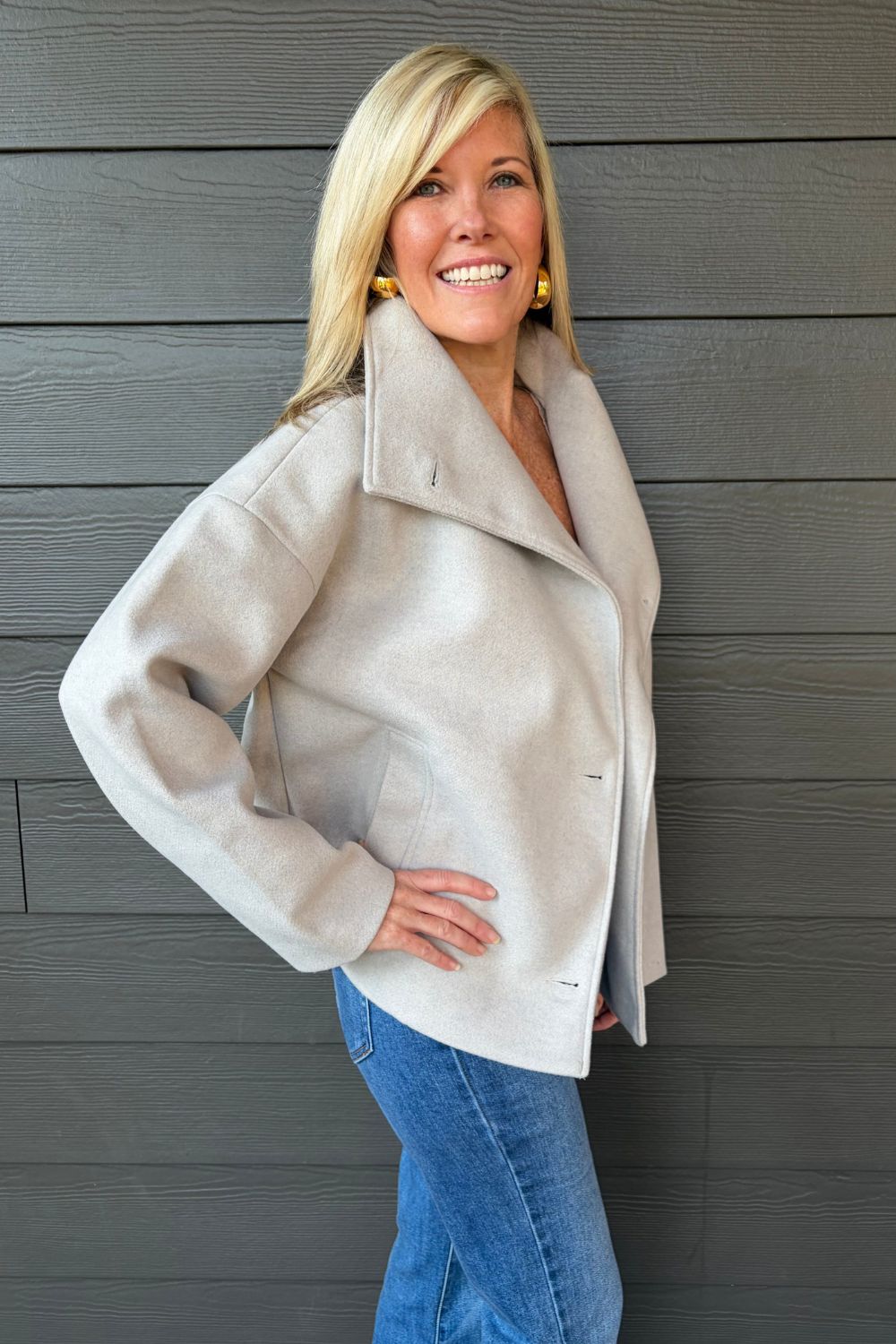 Woman wearing Tribal Sportswear Lofty Chic Funnel Neck Jacket In Antique White with jeans on a dark wood background.