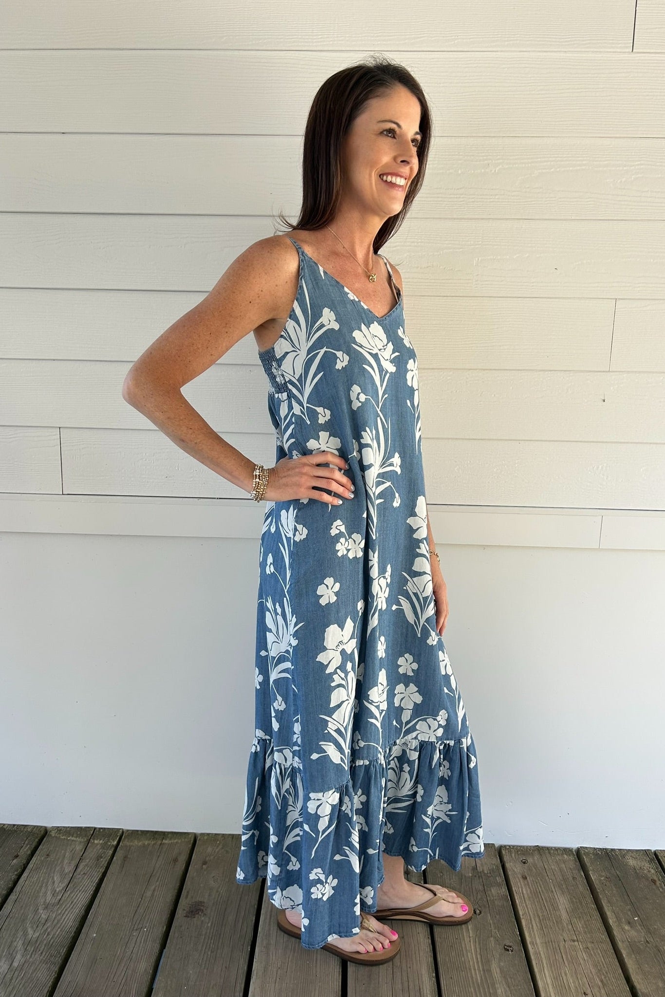 Woman wearing a blue floral dress standing against a white wooden wall.