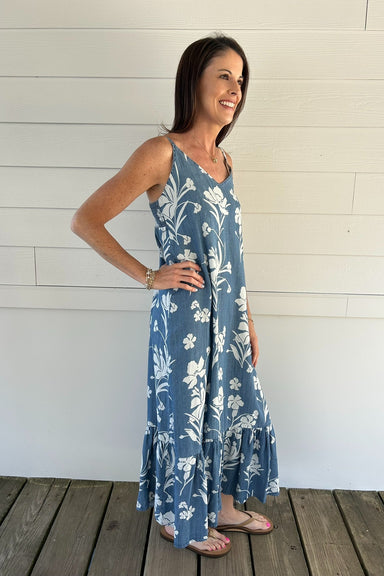 Woman wearing a blue floral dress standing against a white wooden wall.