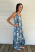 Woman wearing a blue floral dress standing against a white wooden wall.