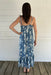 Woman wearing a blue floral dress standing on a wooden deck with a white wall background