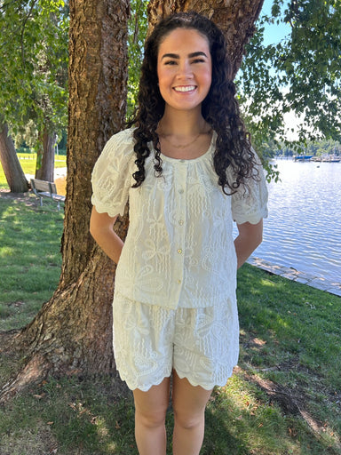 Woman in a light-colored outfit standing by a tree by a body of water