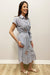 Woman wearing a blue and white stripe dress with embroidery standing against a white wall.