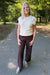A woman standing on an outdoor paved path wearing a cream ribbed short-sleeve knit top, dark brown wide-leg pants, and light gray boots.