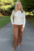 A woman standing on an outdoor paved path wearing a cream long-sleeve button-front cardigan and brown wide-leg corduroy pants.
