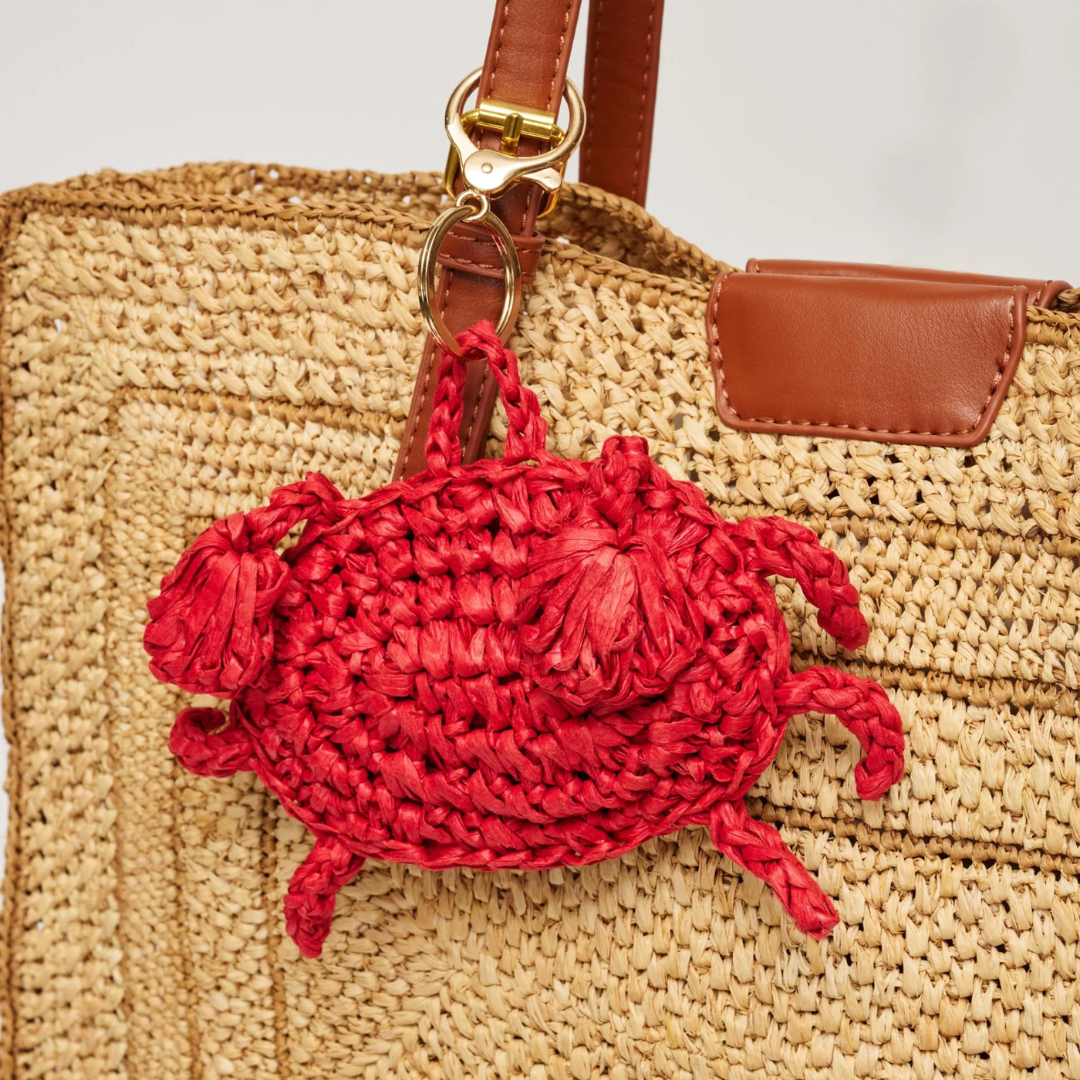 Red crab-shaped keychain attached to a straw bag with brown leather handle.