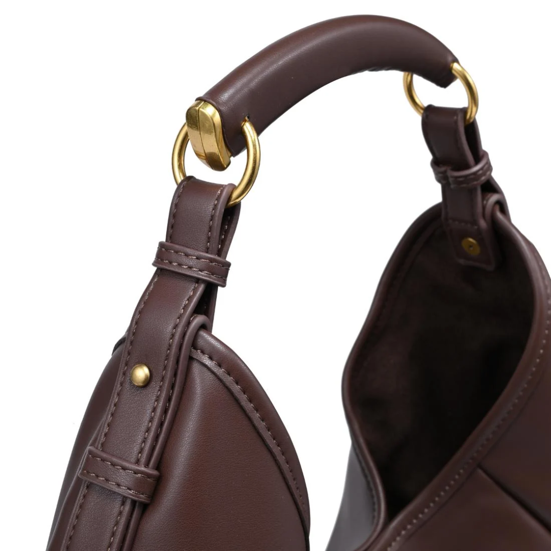 Close-up of a dark brown leather shoulder bag with gold-tone hardware, showing the curved top handle, strap attachment, and interior opening on a white background.