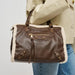 A brown faux-leather shoulder bag with white shearling lining, carried by a model wearing a beige trench coat and blue jeans.