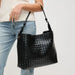 A black woven leather shoulder bag with a top handle, carried by a model wearing a cream top and light blue jeans against a plain white background.
