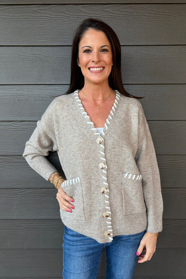 Woman wearing Very Moda Contrast Whipstitch Cardigan In Khaki with jeans on a dark wood background.