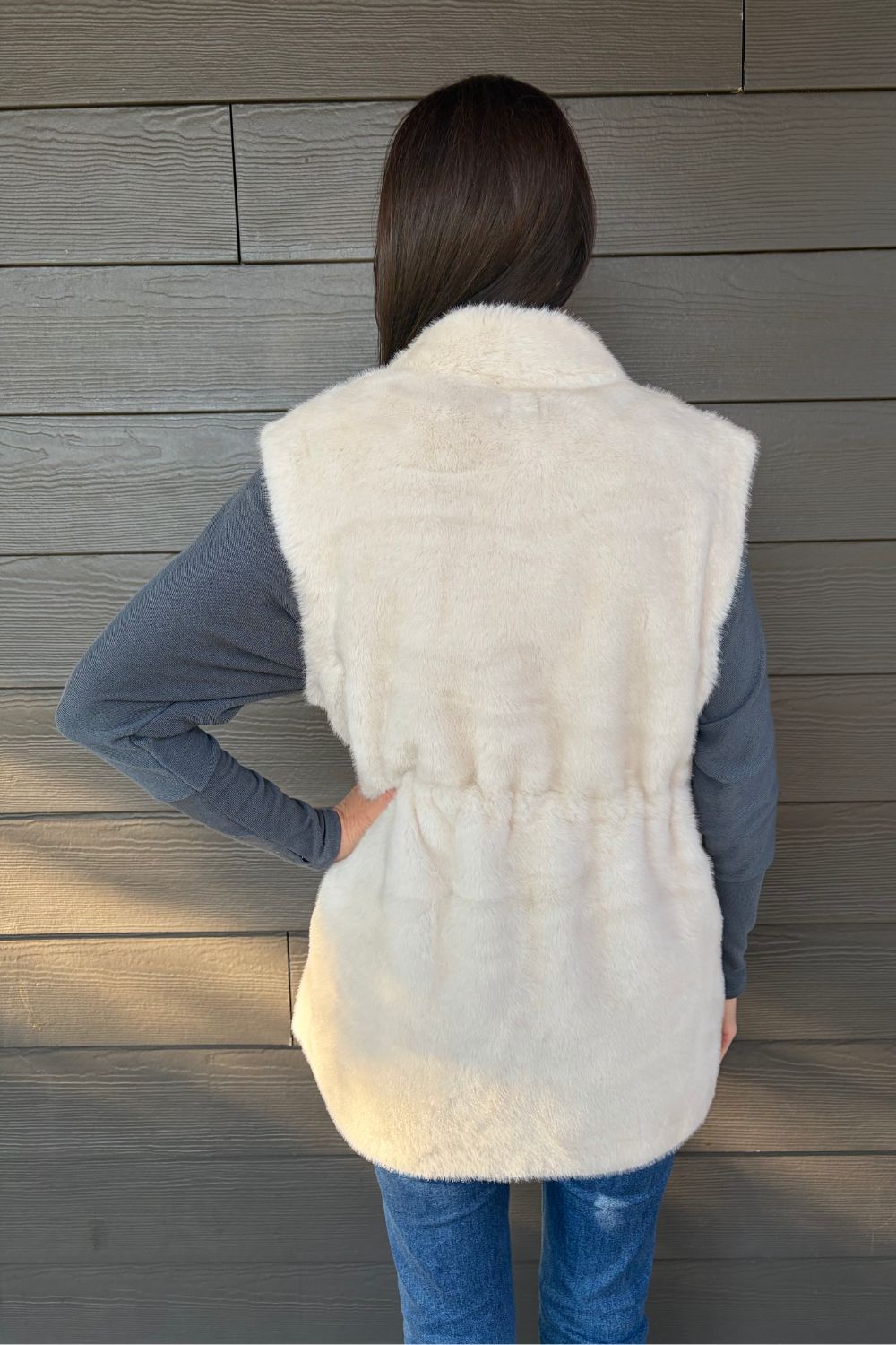 Woman wearing Very Moda Fur Snap Vest In White with jeans on a dark wood background.