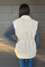 Woman wearing Very Moda Fur Snap Vest In White with jeans on a dark wood background.