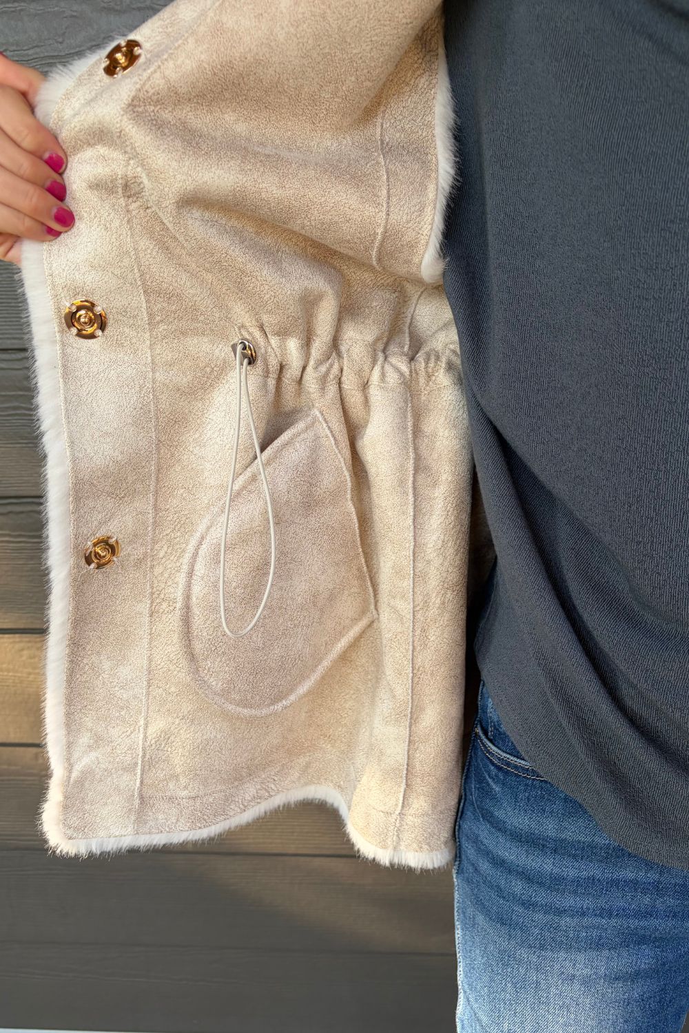 Woman wearing Very Moda Fur Snap Vest In White with jeans on a dark wood background.