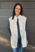 Woman wearing Very Moda Fur Snap Vest In White with jeans on a dark wood background.