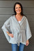 Woman wearing Very Moda Whipstitch Belted Cape In Gray with jeans on a dark wood background.