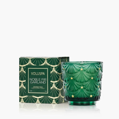 Voluspa Noble Fir Garland scented candle in a green textured glass jar next to its patterned green and gold box, on a white background.