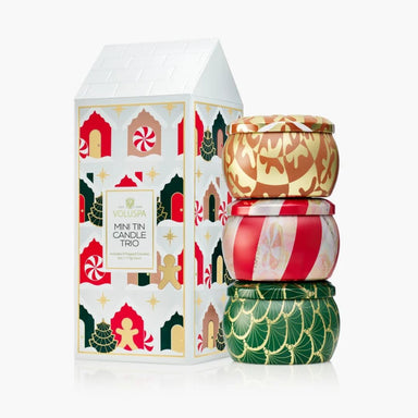 Vollspa Mini Tin Candle Trio set with a white house-shaped gift box decorated with festive gingerbread illustrations, next to three stacked round metal tin candles in gold, red, and green holiday patterns on a white background.