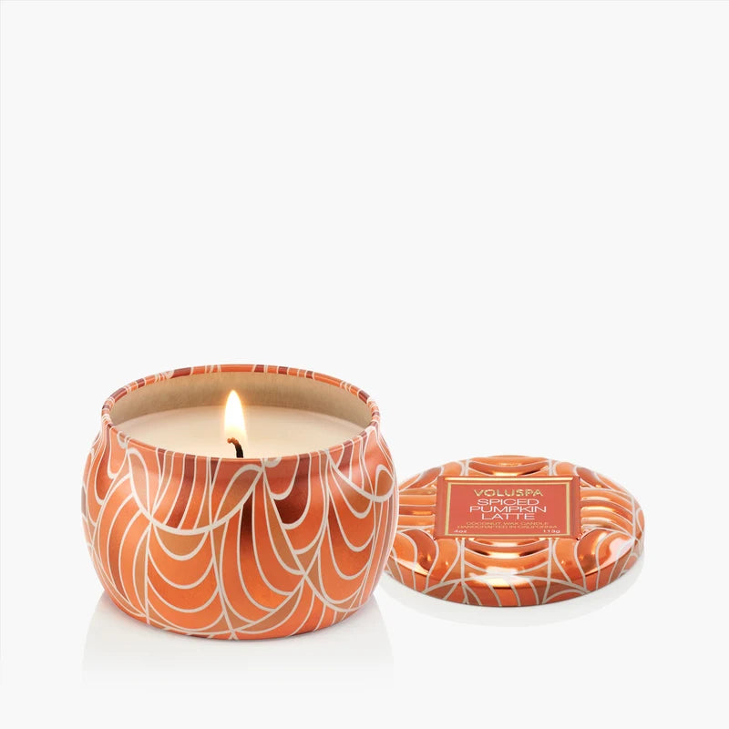 Candle in an orange and white patterned container with a lit candle inside, on a white background.