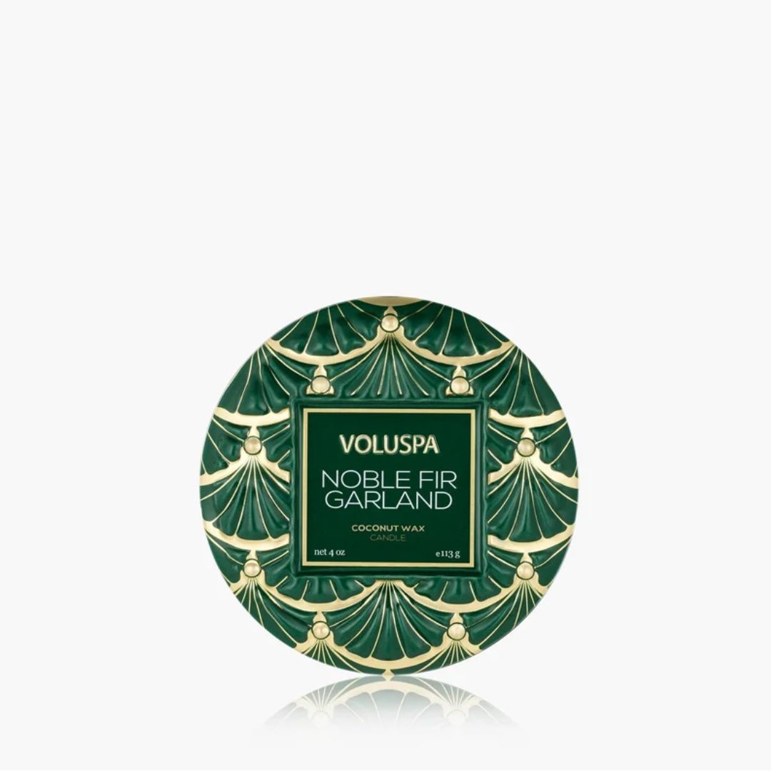 A round green and gold patterned tin of VOLUSPA Noble Fir Garland coconut wax, centered on a light gray background with a soft reflection below.