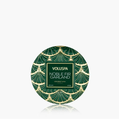 A round green and gold patterned tin of VOLUSPA Noble Fir Garland coconut wax, centered on a light gray background with a soft reflection below.