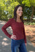 A woman wearing a long-sleeve ribbed button-front top in burgundy and blue jeans, standing outdoors on a paved path with trees in the background.