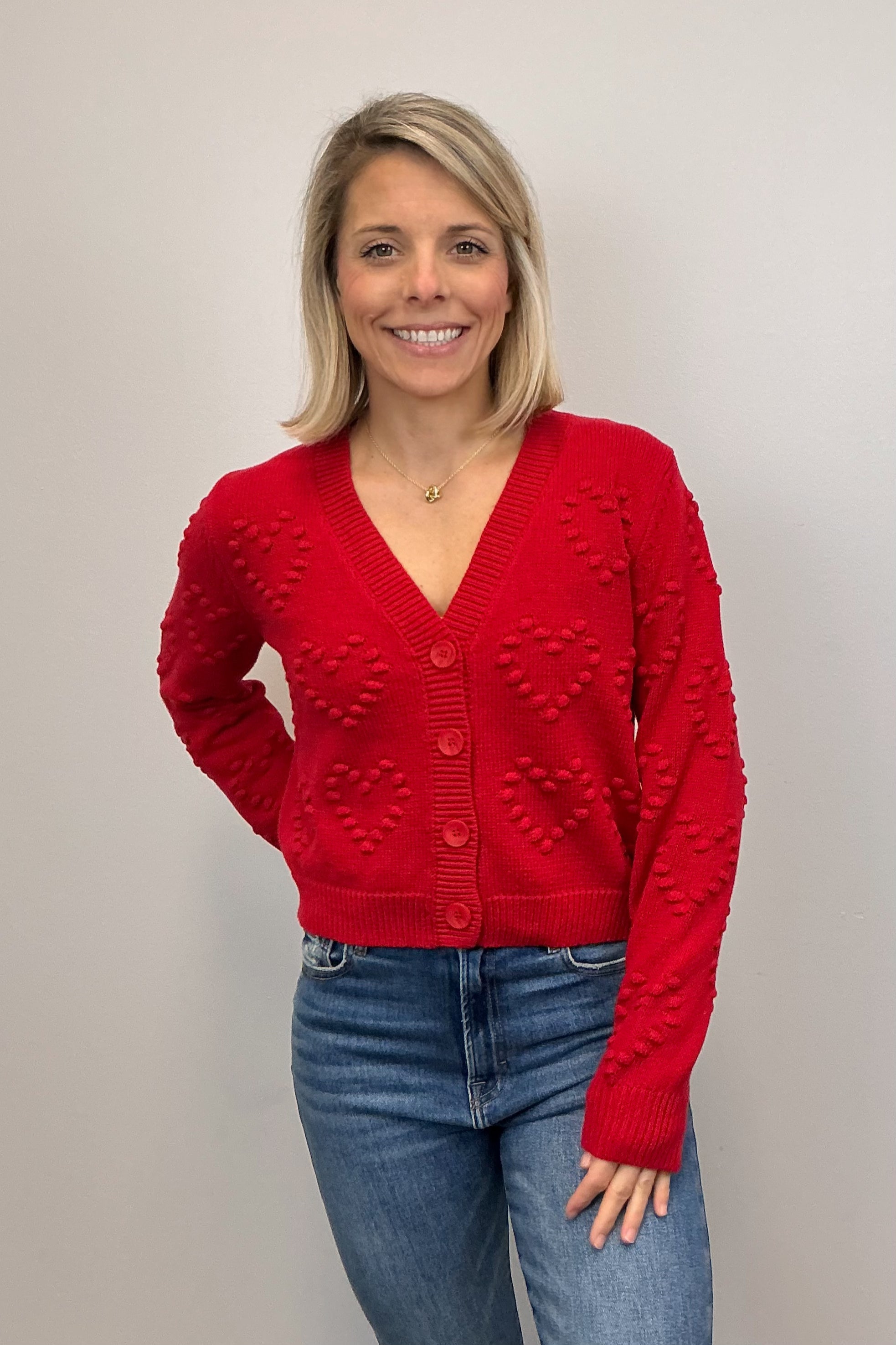 Woman wearing a red cardigan and blue jeans against a plain background