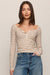 A woman modeling a beige and brown horizontally striped long-sleeve henley top with a wide scoop neckline, paired with blue jeans, against a solid light beige background.