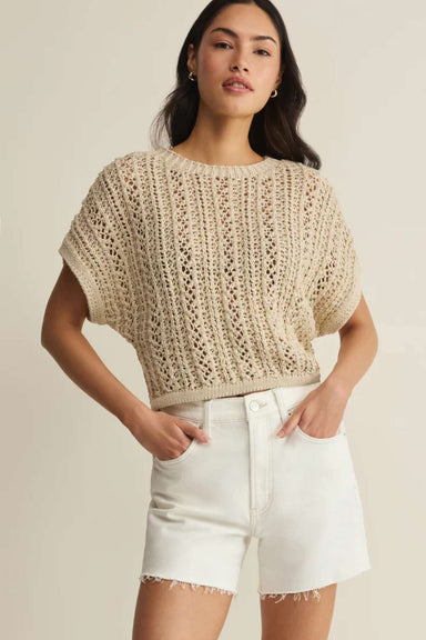 Woman wearing a beige knitted top and white shorts on a neutral background