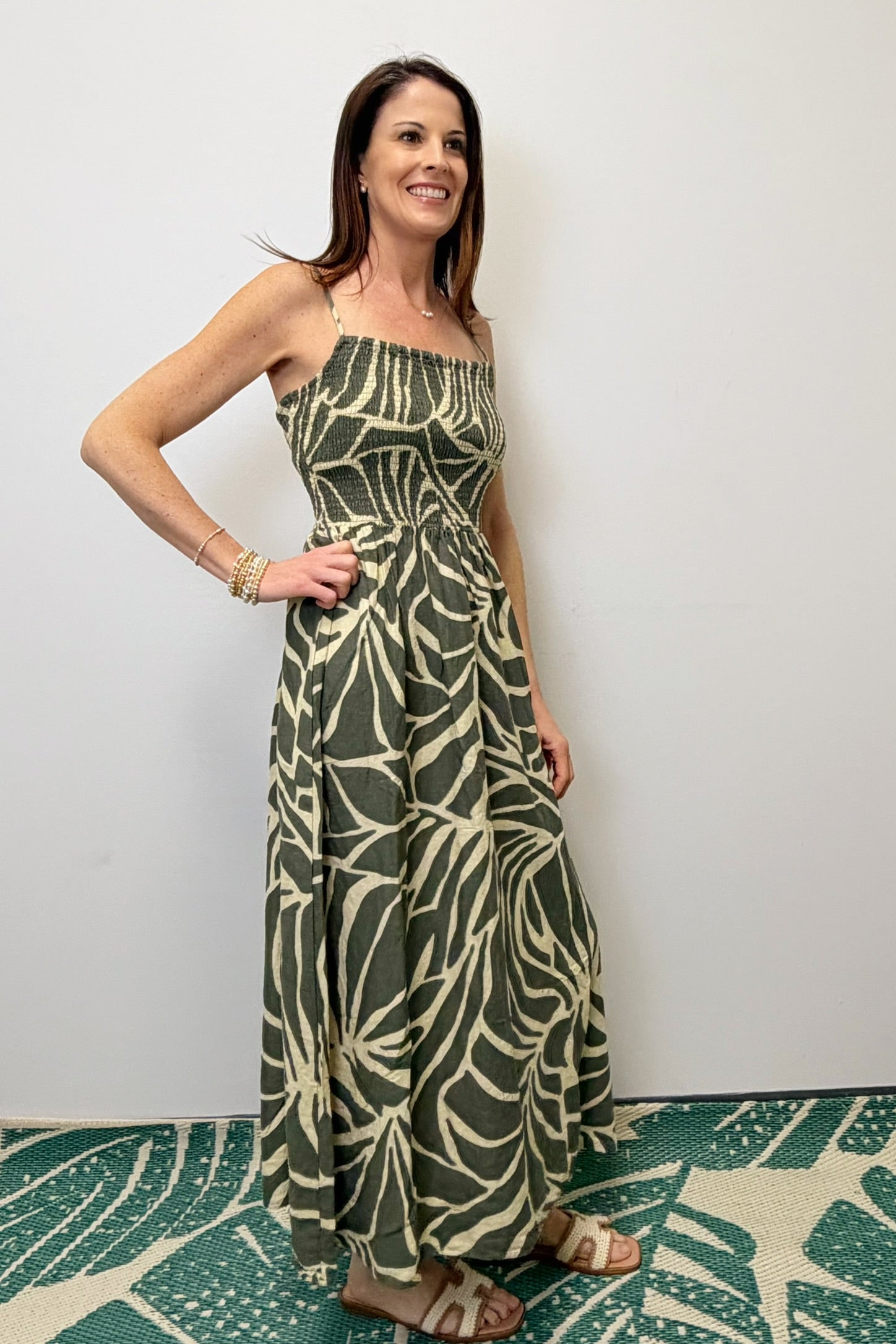 Woman wearing a green and white patterned dress standing against a white wall.