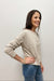 Woman wearing a beige sweater with text and blue jeans against a plain background