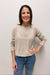 Woman wearing a beige sweater with 'Beach' text and blue jeans against a plain background