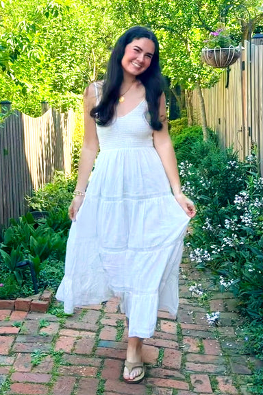 Woman in a white dress standing in a garden with greenery and flowers.