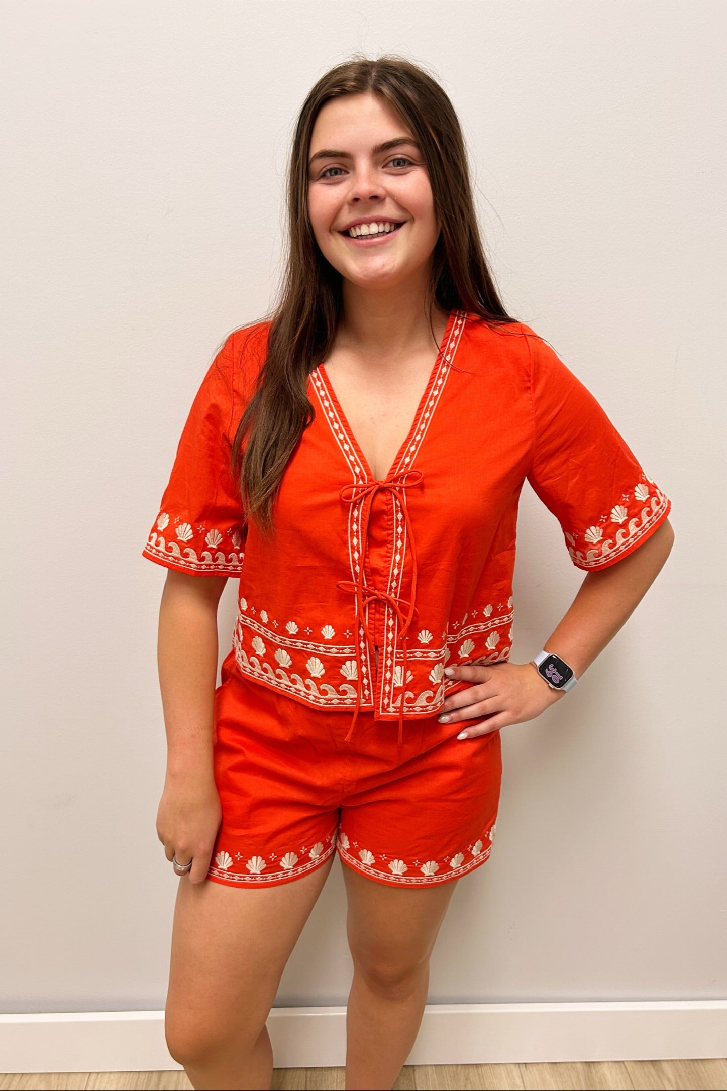 Woman wearing a red embroidered outfit against a plain background
