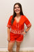 Woman wearing a red embroidered outfit against a plain background