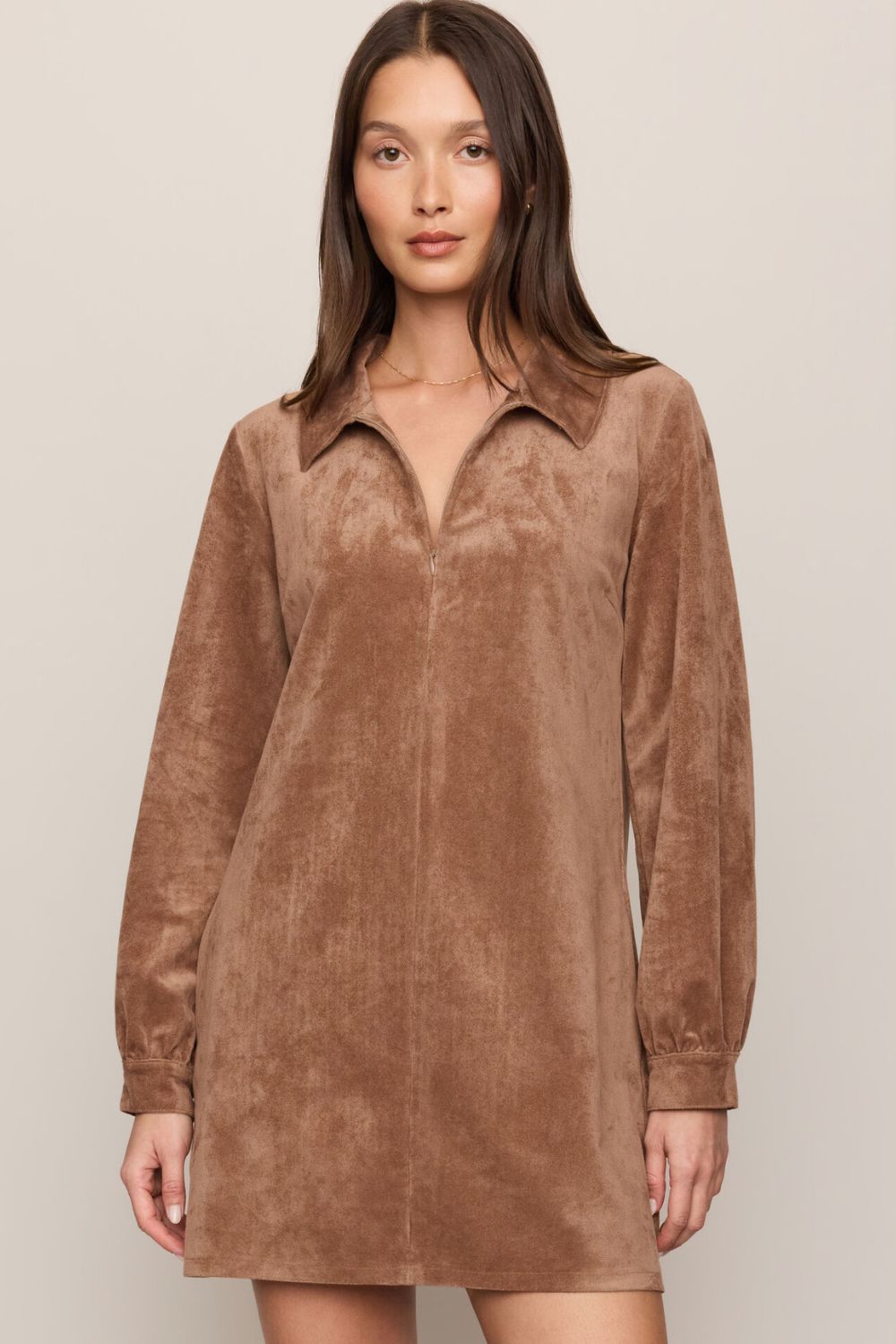 A woman modeling a brown suede long-sleeve collared shirt dress against a plain beige studio background.