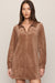 A woman modeling a brown suede long-sleeve collared shirt dress against a plain beige studio background.