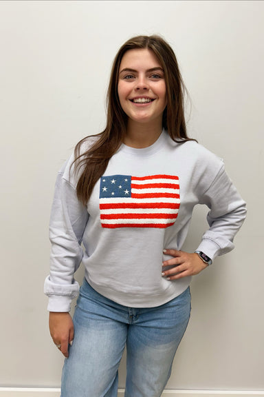 Person wearing a light blue sweatshirt with an American flag design against a plain background
